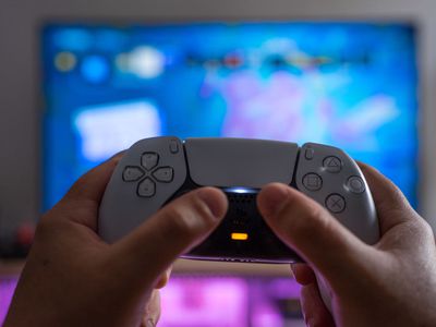 A man holding a PS5 controller in front of a TV.