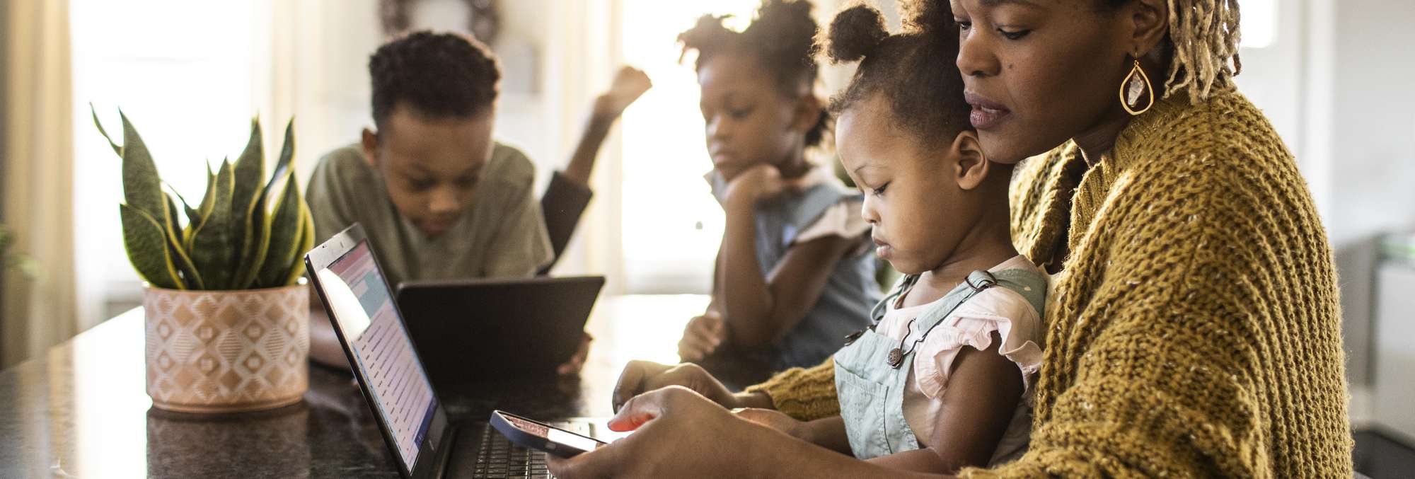 Mother and 3 kids using two laptops and a smartphone