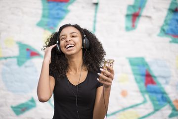 Person listening to a mobile phone with wired headphones and smiling