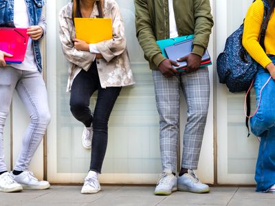 Group of multiracial teenage college students ready to go back to school standing against blue background wall.