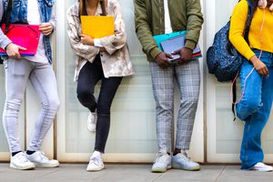 Group of multiracial teenage college students ready to go back to school standing against blue background wall.