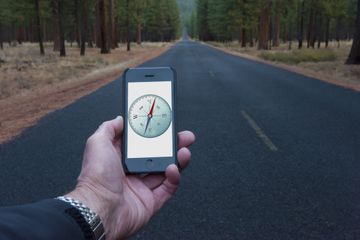 Hand holding compass app on iPhone in front of a long road