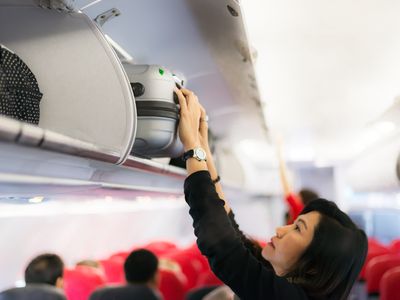 A woman putting a carry on bag in an overhead bin.