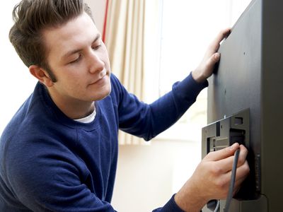 A man in a blue jumper connecting his laptop computer to his TV with an HDMI cable.