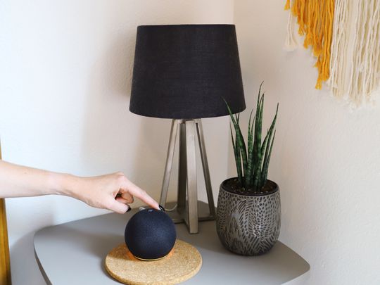 Hand pressing control button on Amazon Echo Dot (5th Gen) displayed on nightstand