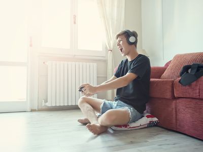 A teenage boy sitting on the floor with a games controller in his hand and headphones on his head