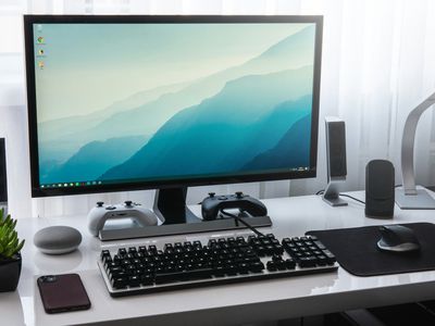 A Windows-based PC sitting on a white desk with black and gray accessories around it. There's a mechanical keyboard in the middle, a smartphone on the left, and a mouse on a black mousepad on the right.