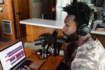 Someone recording a podcast at a table in the dining room, with a laptop computer and microphone.