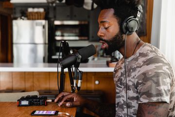 Someone wearing headphones and speaking into a microphone recording their voice on a smartphone.