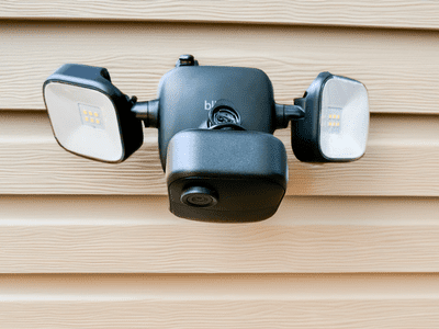 Blink Outdoor 4 Floodlight camera on light colored vinyl siding.